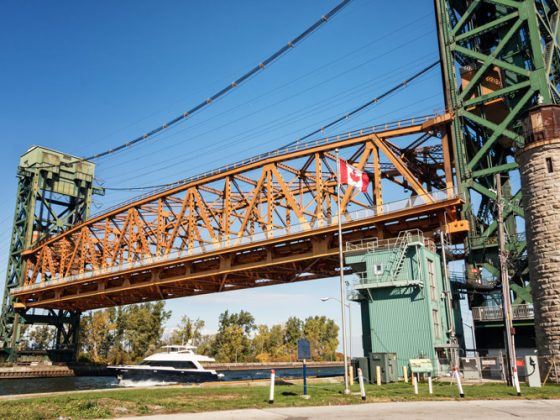 A lift bridge spanning a canal with its deck raised to allow a boat to pass underneath.