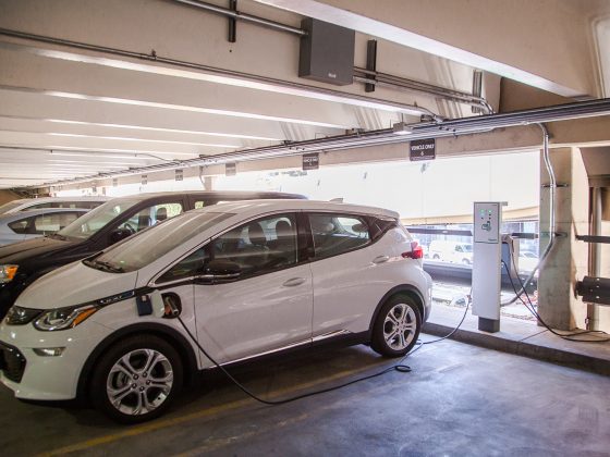 A white car is plugged into an electronic vehicle charging station in a parking garage.