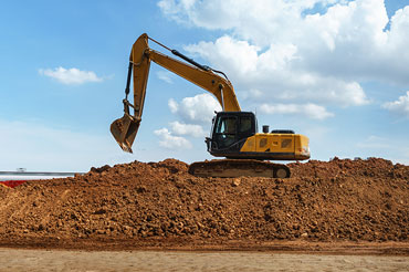 An excavator sits atop a large excess soil mound.