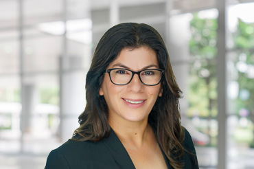 A woman wearing glasses dressed in a black suit jacket with a black shirt.