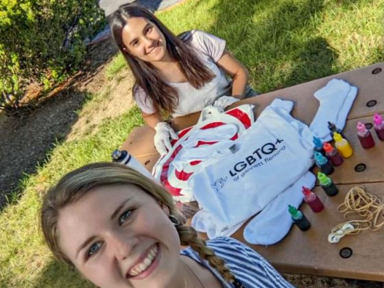 Two young women smile for a selfie as they tie-dye LGBTQ+ of Gannett Fleming t-shirts.