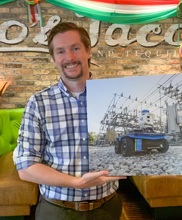 A man is standing, holding a picture of a robot in a power transmission substation.