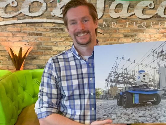 A man is standing, holding a picture of a robot in a power transmission substation.