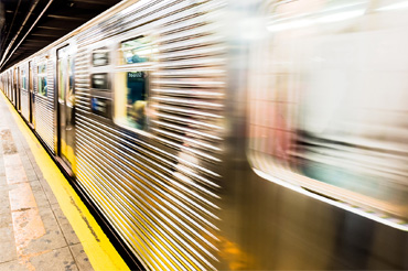 A New York City subway train passes through a station. The train is in motion, blurring the image.