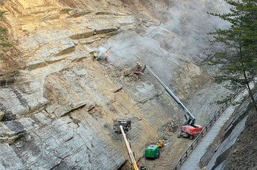 A construction crew repairs a rock wall with lift cranes and other machinery.