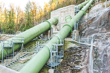 Two large green pipes are attached to a steep rocky hillside.