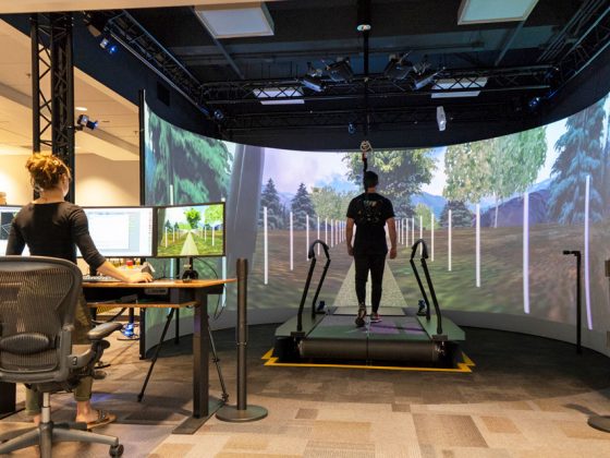 A woman stands behind computer screens and analyzes a man walking on a treadmill at Penn State’s Biomechanics Lab.