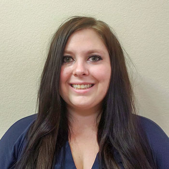 Stephanie standing in front of a tan wall smiling for the camera.