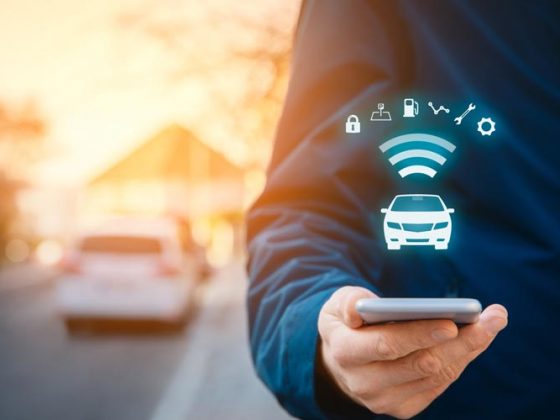 Image of a man holding a cell phone in the foreground. The cell phone depicts icons that show the phone is wirelessly connected to the car in the background.