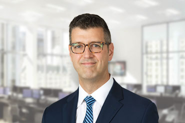 Man wearing glasses and a blue suit smiles for a portrait.