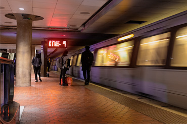 A subway station with rider waiting on the platform with a blurred train moving by.